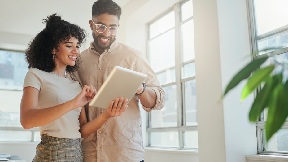 Foto com a imagem de dois colaboradores felizes olhando para um tablet.