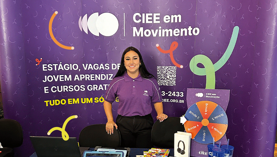 Foto com uma mulher em pé e sorrindo em frente a um banner do CIEE em movimento.