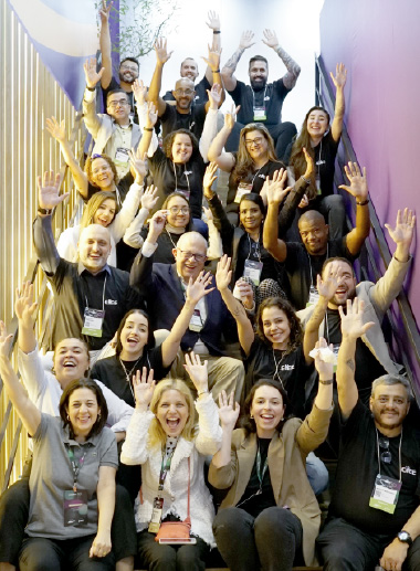 Foto dos participantes alinhados em uma escada, todos de braços levantados e sorrindo para a foto