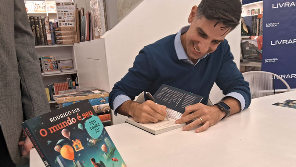 Rodrio Dib, autor do livro, escrevendo uma dedicatória na obra em cima de uma mesa branca