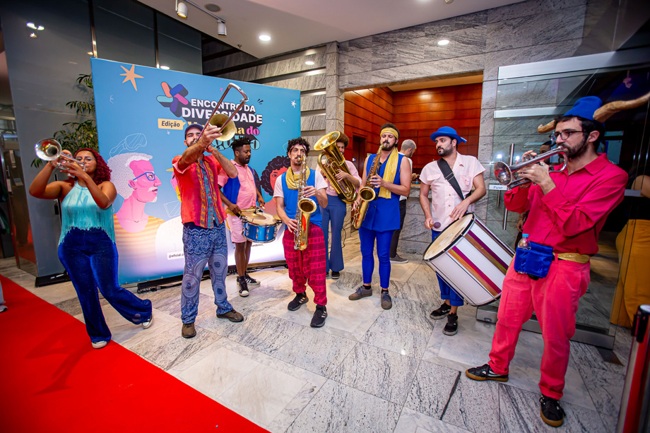 Uma equipe de homens vestindo roupas vermelhas e azuis tocando instrumentos no saguão do Espaço CIEE