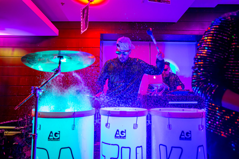 Homem tocando em uma bateria, há agua no instrumento, causando um efeito na foto enquanto ele utiliza o instrumento a água sobe.