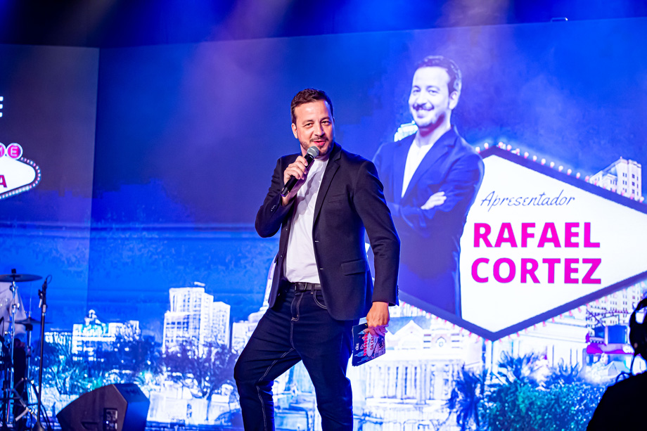 Homem com vestes sociais, segurando um microfone, em cima do palco do Espaço CIEE