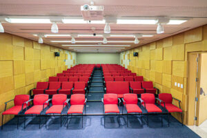 Diversas cadeiras vermelhas vazias em um auditório com paredes amarelas