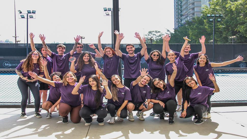 Grupo de 18 jovens, todos vestindo camisetas roxas com o logotipo do CIEE, posam sorridentes para a foto em uma quadra esportiva ao ar livre.