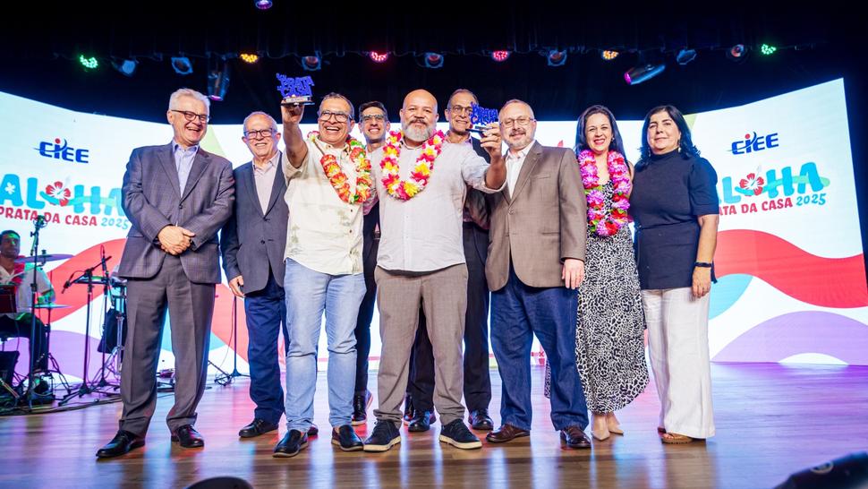 Diversas pessoas vestidas em clima Aloha em cima do palco segurando o Prêmio