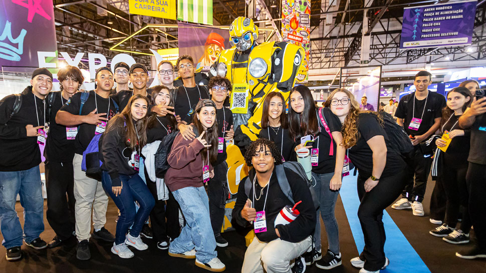 Jovens posando ao lado de um robô amarelo de quase dois metros