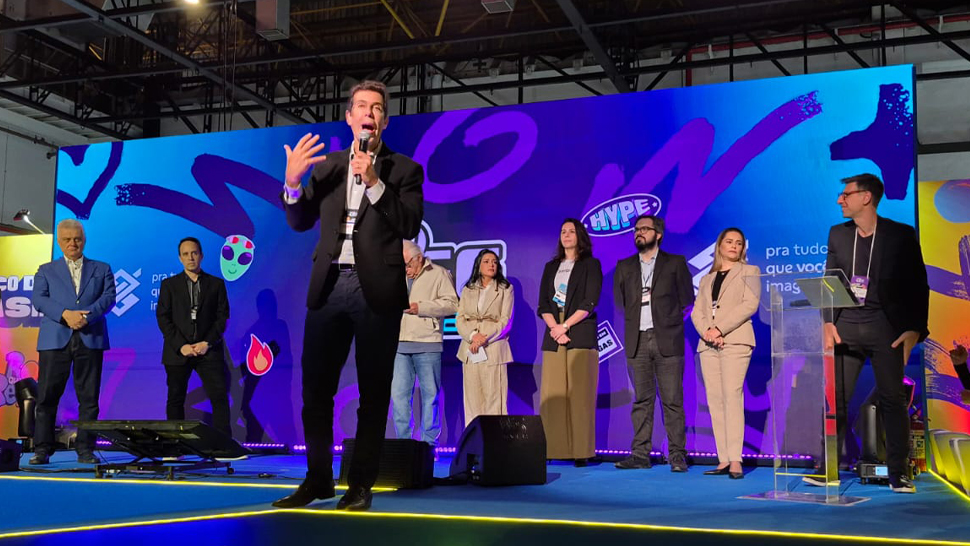 Palco do banco do Brasil com decoração amarela, telão azul no fundo, cerca de 9 autoridades acompanham com roupas sociais a abertura do evento